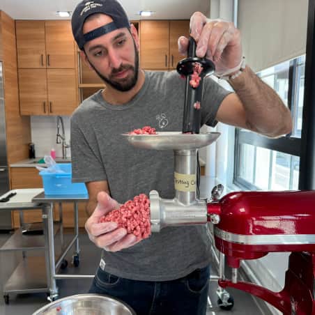 A man pushing meat through a Kitchenaid meat grinder attachment